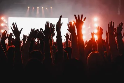 Fans silhouetted with hands raised in red concert glow backdrop Stock Photos