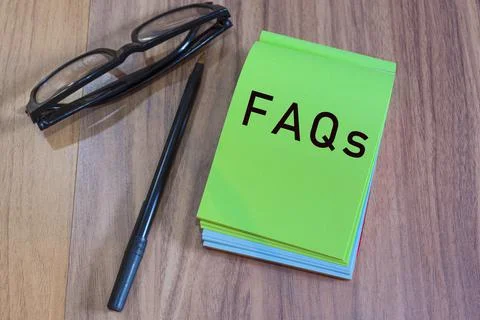 FAQs text on green notepad with glasses and pen on a desk Stock Photos