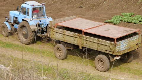 Farm Tractor with a Utility Trailer Passing on an Unpaved Rural Road Stockbeeldmateriaal 89905978