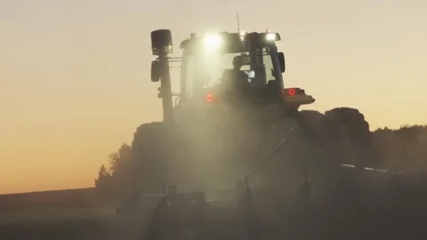 Farm Tractor Working Through Dust At Sunset With Sun Rays And Warm Golden L.. Stock Footage 336943466