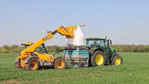 Farm worker with a telehandler loading fertiliser into a fertiliser spreader. UK Stock Footage 183863129