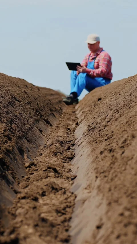 Farmer, agronomist sits between special soil rows on field. he tests, using Stock Footage 314840730