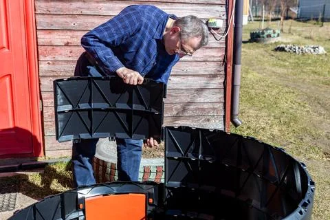 Farmer assembling modular compost bin from plastic segments in backyard. Stock Photos