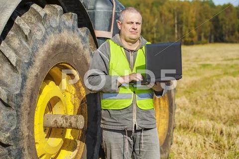 Farmer with computer near the tractor on field Stock Photos