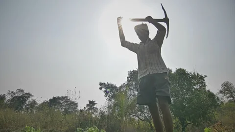 A farmer digging up the soil with Pickax against the afternoon hard sun Stock Footage 90105649