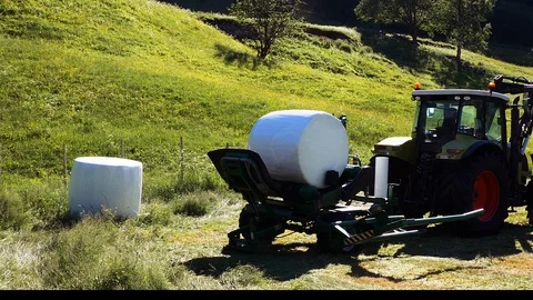 Farmer drops a white wrapped round hay bale at the edge of the field. Stock Footage 119322805
