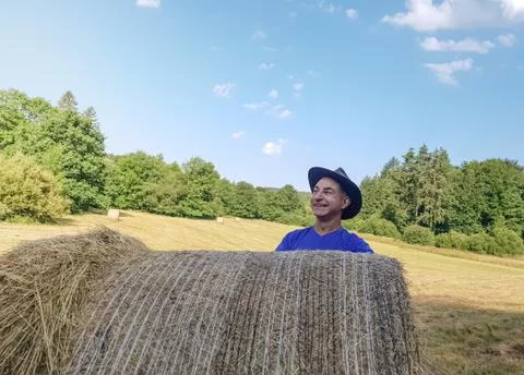 A farmer in a hat stands at a stack of fresh hay Stock Photos