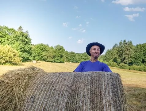 A farmer in a hat stands at a stack of fresh hay Stock Photos