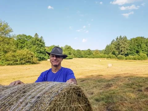 A farmer in a hat stands at a stack of fresh hay Stock Photos