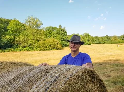 A farmer in a hat stands at a stack of fresh hay Stock Photos