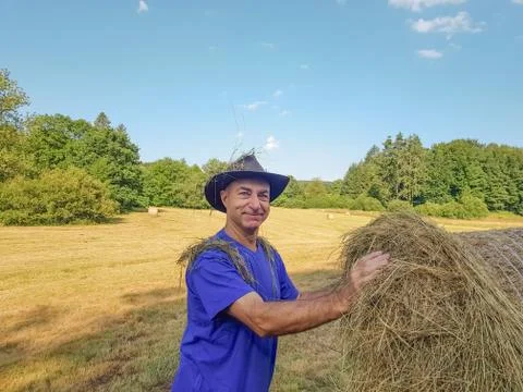 A farmer in a hat stands at a stack of fresh hay Stock Photos