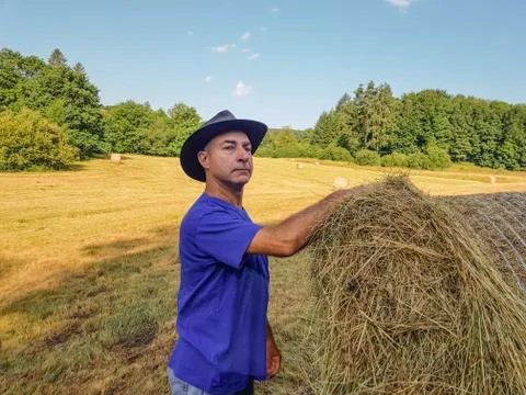A farmer in a hat stands at a stack of fresh hay Stock Photos