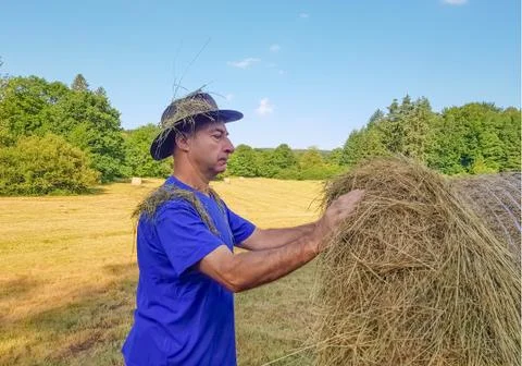 A farmer in a hat stands at a stack of fresh hay Stock Photos