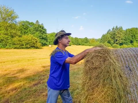 A farmer in a hat stands at a stack of fresh hay Stock Photos
