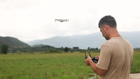 Farmer holds drone control panel.Quadcopter flies over green rice fields Video stock 322043565