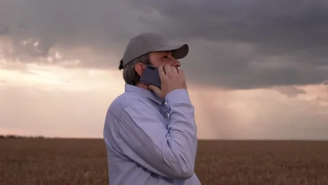 Farmer man in wheat field talking on mobile phone. Rain cloud over wheat field Stock Footage 310517978