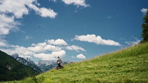 Farmer mows grass on a small alpine farm while working under a blue sky and Stock Footage 344146657