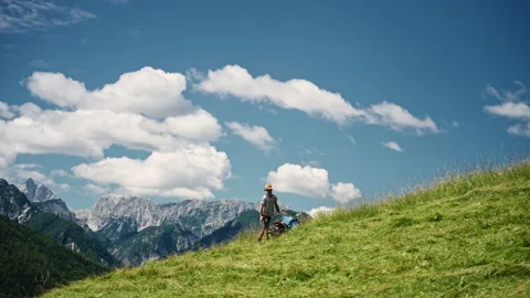 Farmer mows grass on a small alpine farm while working hard under the blue sky Stock Footage 344150382