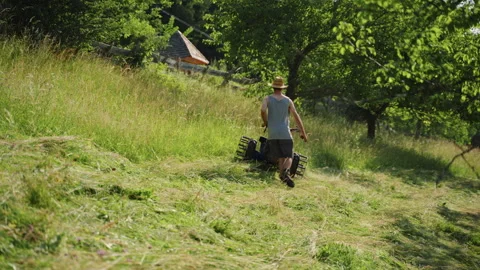 Farmer mows grass on a small alpine farm in summer sun while working hard Stock Footage 344151534