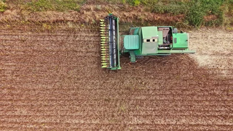 Farmer operating a green combine harvester in a field during daylight hours Stock Footage 345454080
