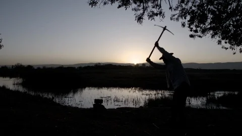 Farmer with a pickaxe makes a hole in the ground for planting seedlings Stock Footage 122073293