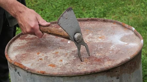 Farmer piercing rusty metal drum lid with grub hoe tool Video stock 335546407