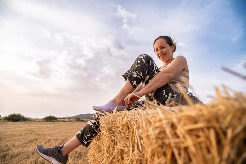 Farmer putting on socks while sitting on hay bale in field at sunset Stock Photos