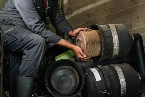 Farmer replacing air filter of tractor engine in workshop Stock Photos