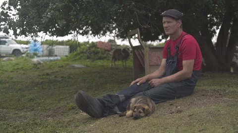Farmer sitting on the grass next to a cute puppy. Stock Footage 247523584