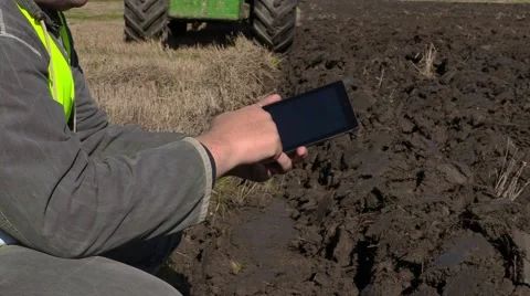 Farmer with tablet PC near moving tractor on field Stock Footage