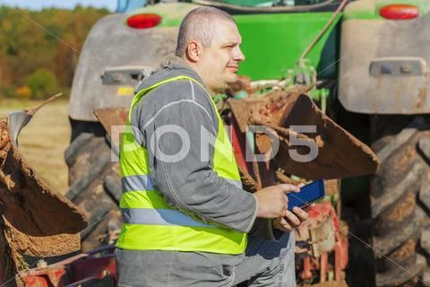 Farmer with tablet PC near tractor on field Stock Photos