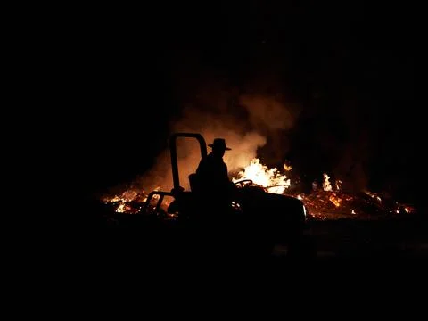 Farmer on tractor back-burning against bushfire, night bush fire Stock Photos