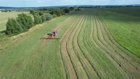 The farmer turns the grass with a hay rake attached to the tractor. Shot from a Stock Footage 167049702