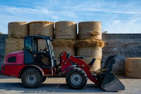 Farmer unloading round bales of straw with a front end loader Stock Photos