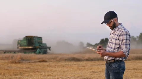 Farmer uses a digital tablet in the background of a working combine Stock Footage 115936683
