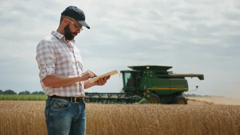 A farmer uses a digital tablet, in the background is a harvester Stock Footage 136294061