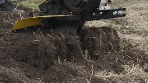 A farmer uses a walk-behind tractor to plow a farm plot, preparing fertile soil Vídeos de archivo 312580334