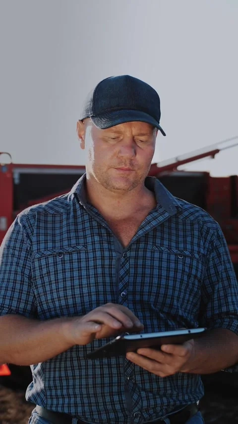 Farmer using digital tablet. on farm field, on farm machinery backdrop. tractor Stock Footage 314564742
