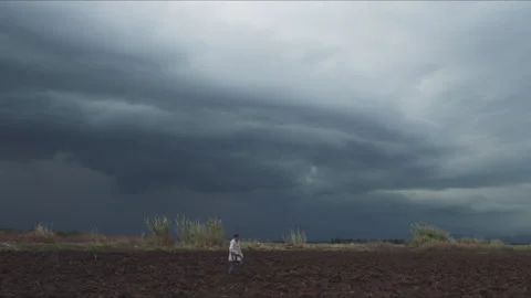 Farmer walking in a plowed field under a dark stormy sky Stock Footage 330564856