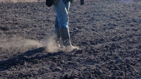 A farmer walks through a plowed field, dust flying from under his boots. Stock Footage 195873526