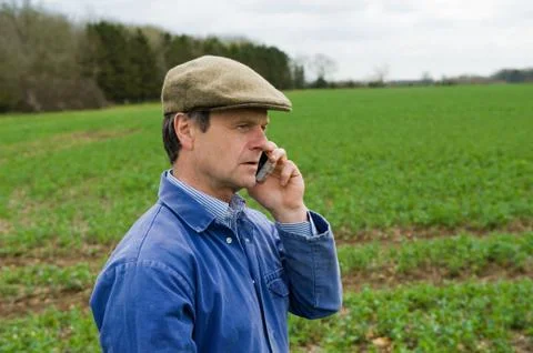 Farmer wearing flat cap talking in field on smartphone 写真素材
