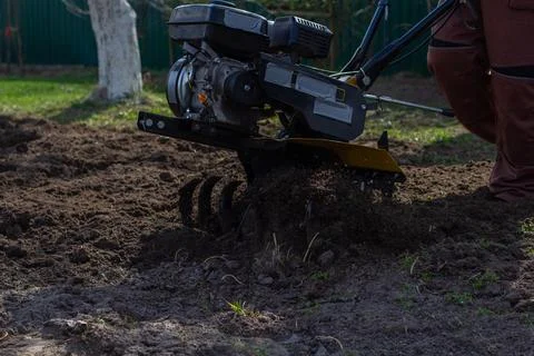 Farmer in work clothes operating a motor cultivator tilling soil in a home Foto stock