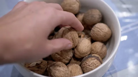 Farmer's Hand Taking One Walnut from a Full Bowl of Harvested Nuts. Close-up Stock Footage 236067230