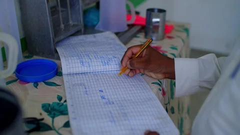 Farmer’s hand writes figures in a grid ledger on a patterned table beside Stock Footage 345729831