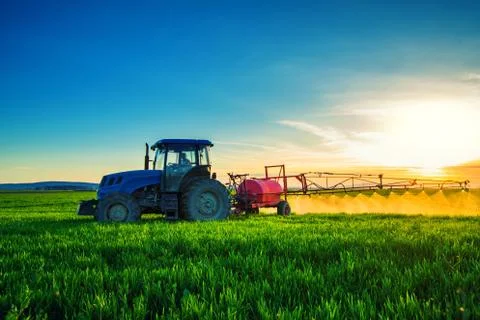 Farming tractor plowing and spraying on field Stock Photos