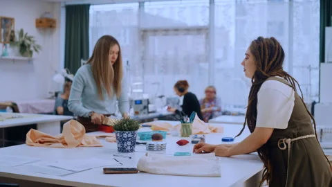 Fashion designer with dreadlocks discussing work with colleague in sewing studio Vídeos de archivo 335932433