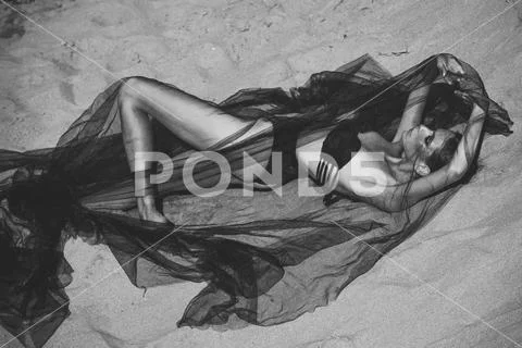 Fashion woman in swimsuit under black veil relax on sand Stock Photos