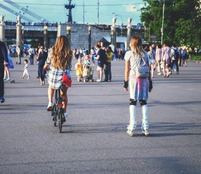 Fashionable beautiful girls on rollers and on a bicycle in the park Stock Photos