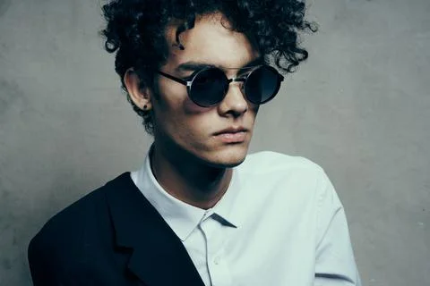 Fashionable curly haired brunet guy in a shirt with glasses and a jacket on his Stock Photos