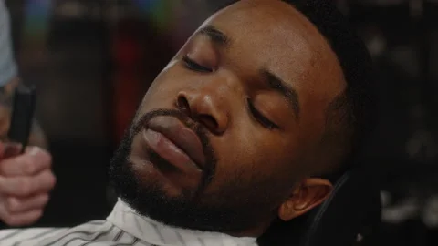 Fashionable dark-skinned guy gets a beautiful beard hairstyle in a barbershop Stock Footage 170596749
